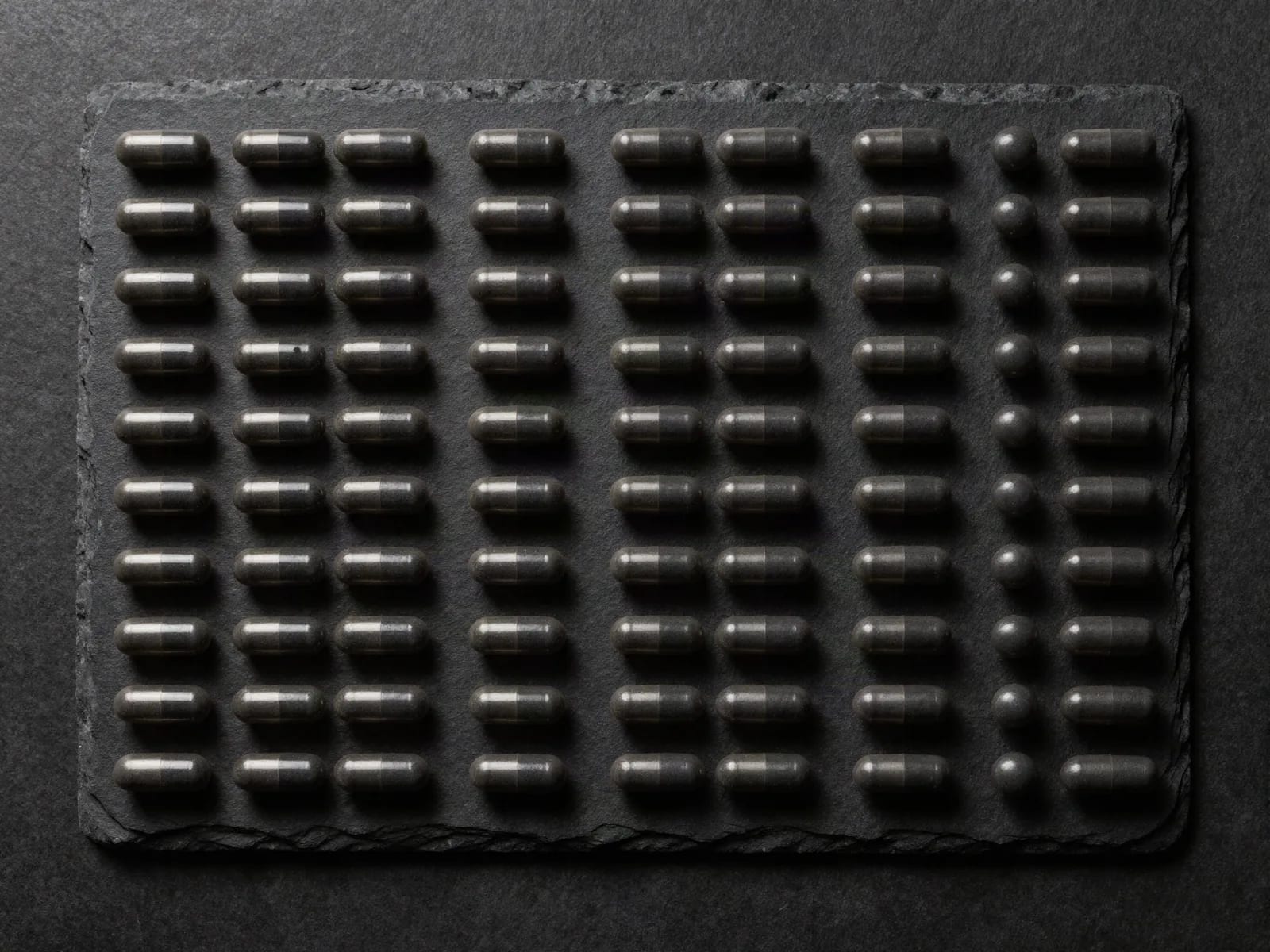 Dark capsules laid out in a complete, precise grid on black slate